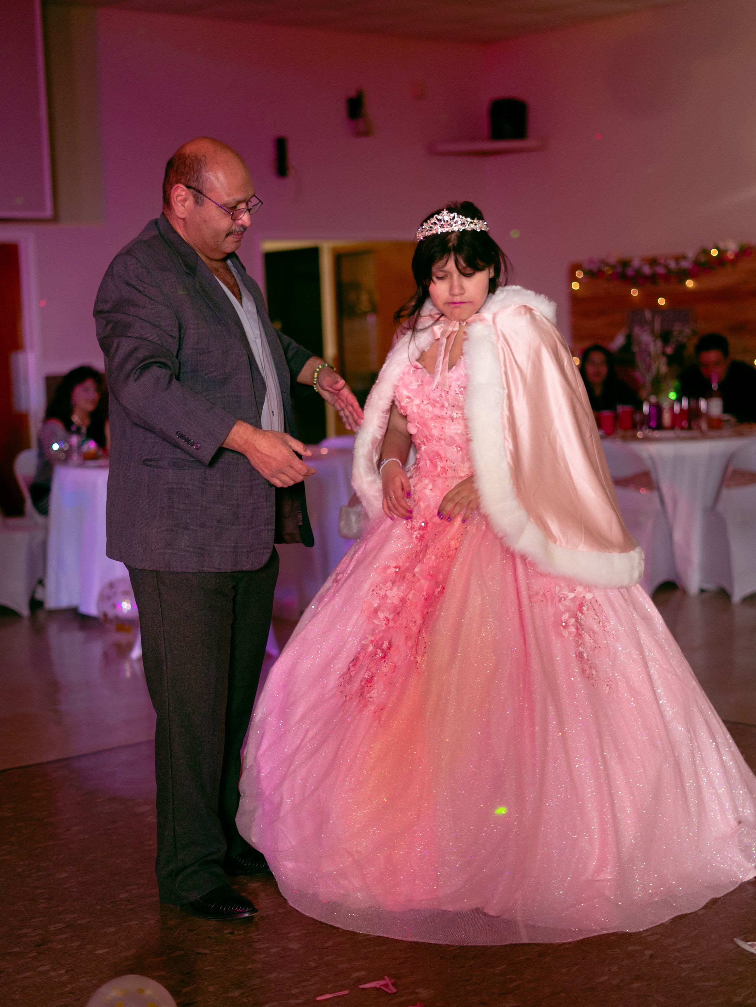 Traditional quinceañera dance moment in an elegant reception hall with pink decor.