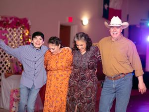 A group of four people dancing in a line at a party with a decorative pink backdrop.