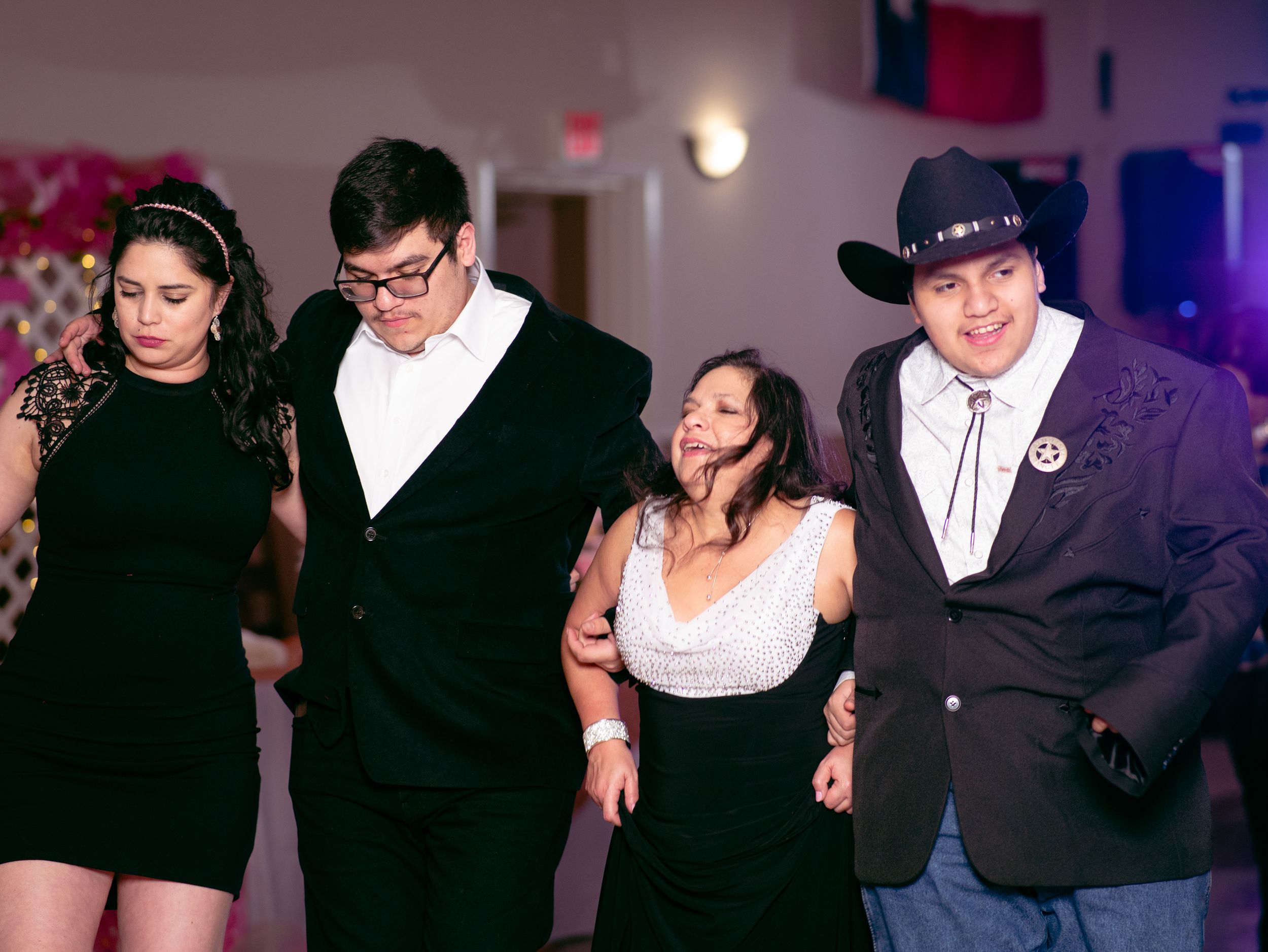 Four people arm in arm dancing in formal attire at a celebration event.