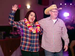A couple dancing at a party, with one wearing a plaid shirt and lei, the other in a cowboy hat.