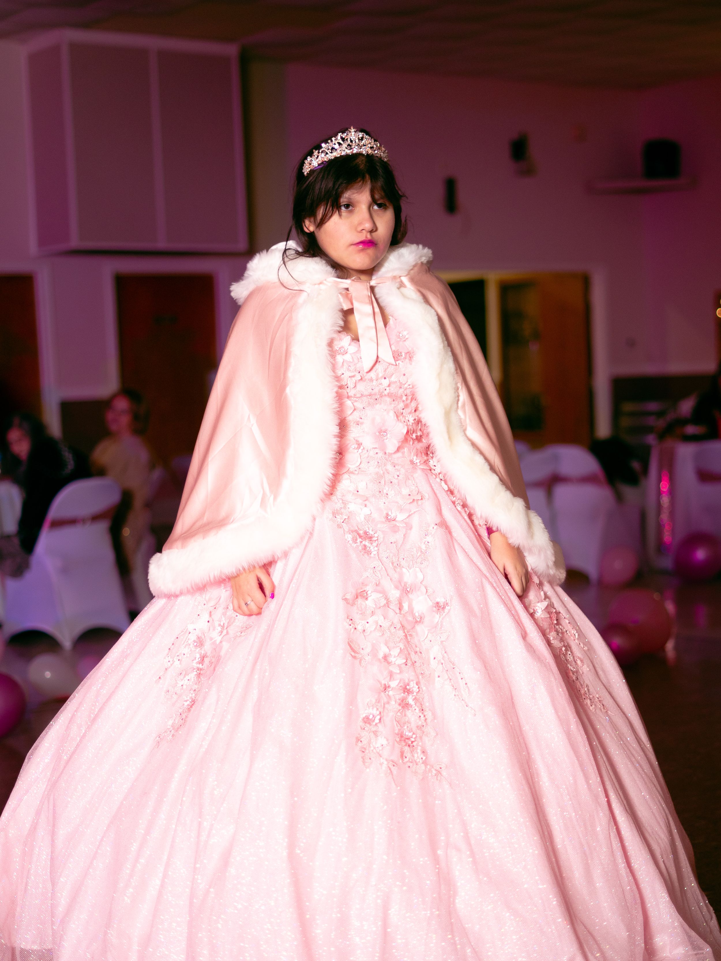 Young woman in a pink princess ball gown and tiara at her quinceañera celebration.