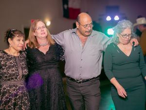 Four individuals dancing together at a celebration with colorful lighting in the background.
