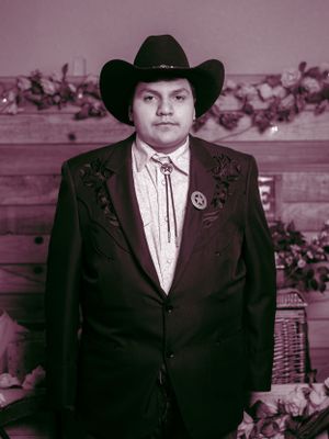 A formal portrait of a person wearing a black suit jacket, western tie, and cowboy hat against a floral backdrop.