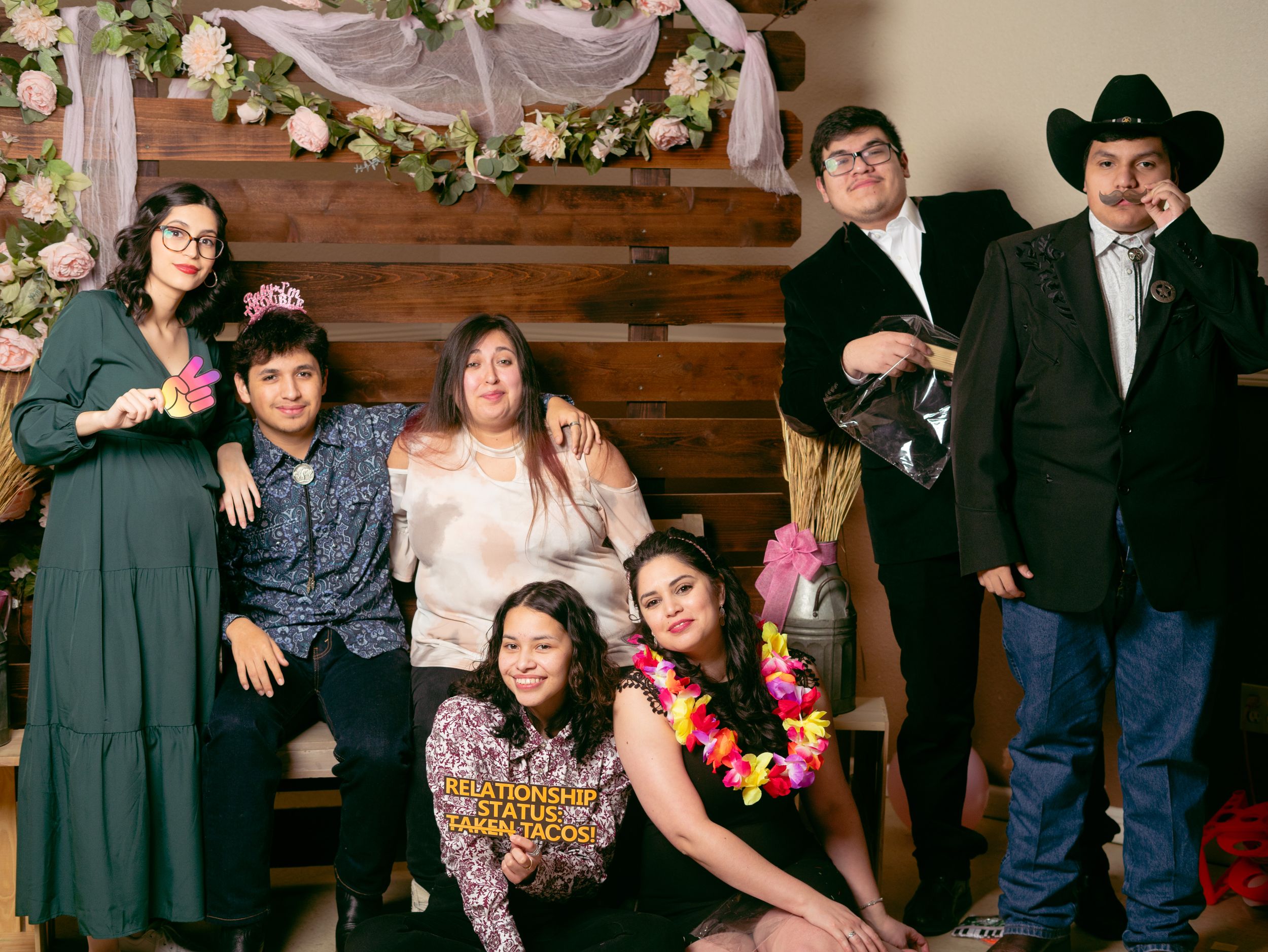 A formal family portrait in front of a wooden backdrop decorated with white flowers and ribbons.