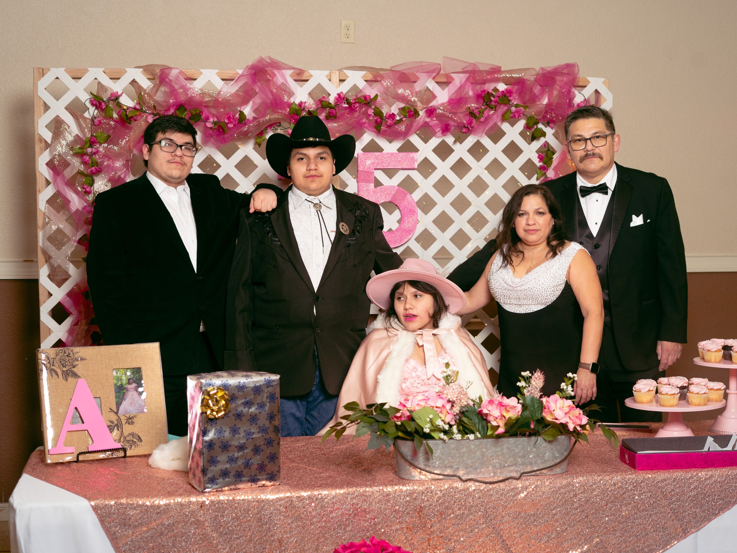 A formal group photo against a pink lattice backdrop at a celebration event.