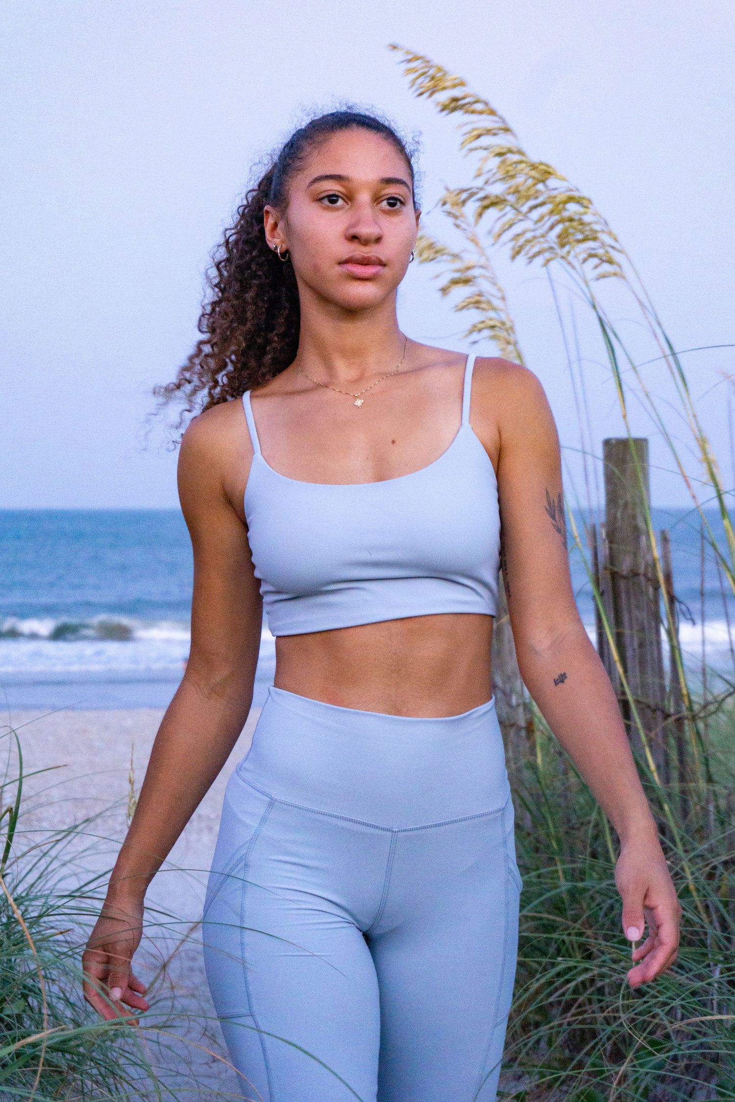 A girl walks on the beach in lilac light purple yoga athletic wear sports bra and leggings