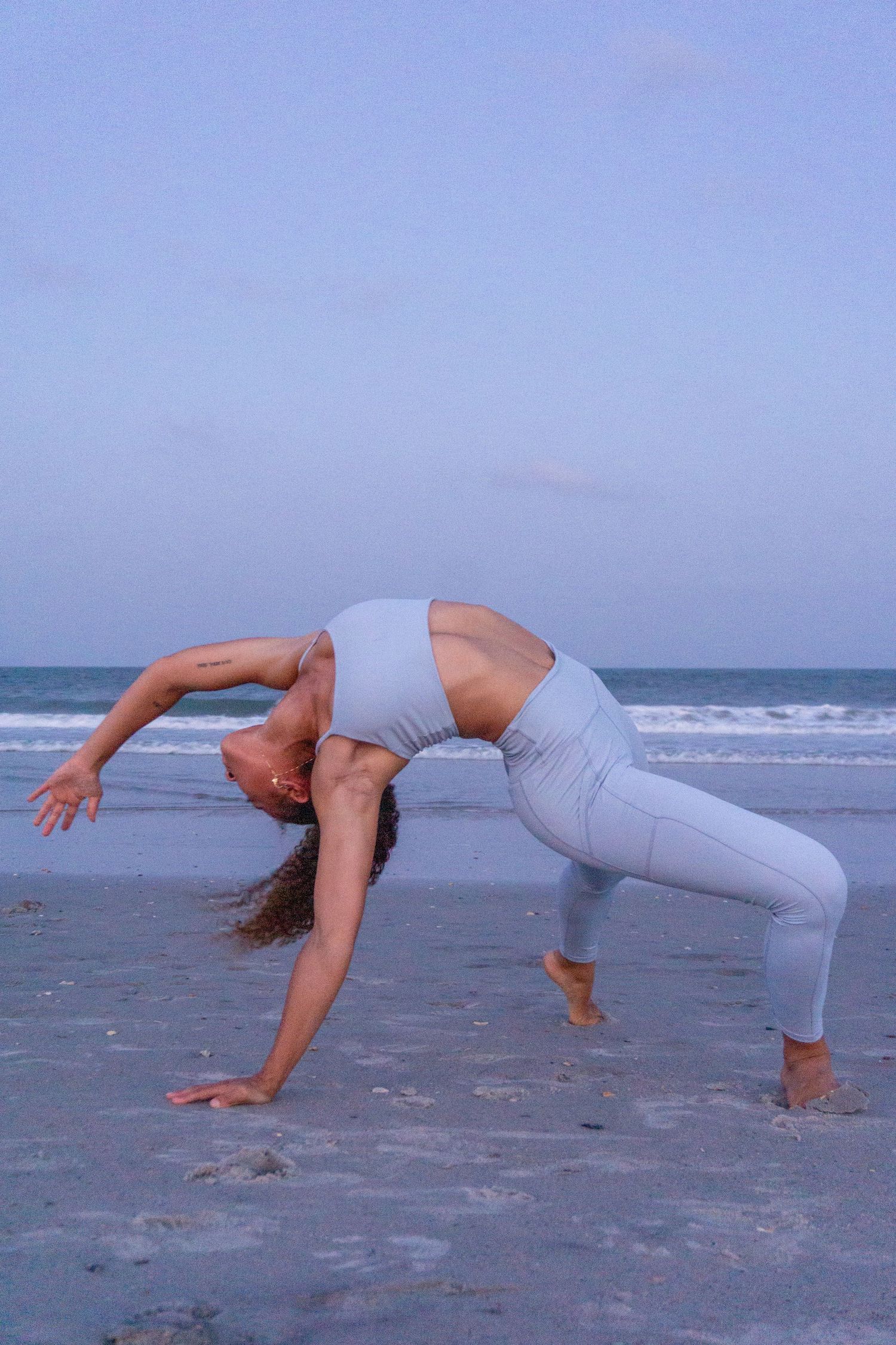 A girl yoga poses on the beach in lilac light purple yoga athletic wear sports bra and leggings