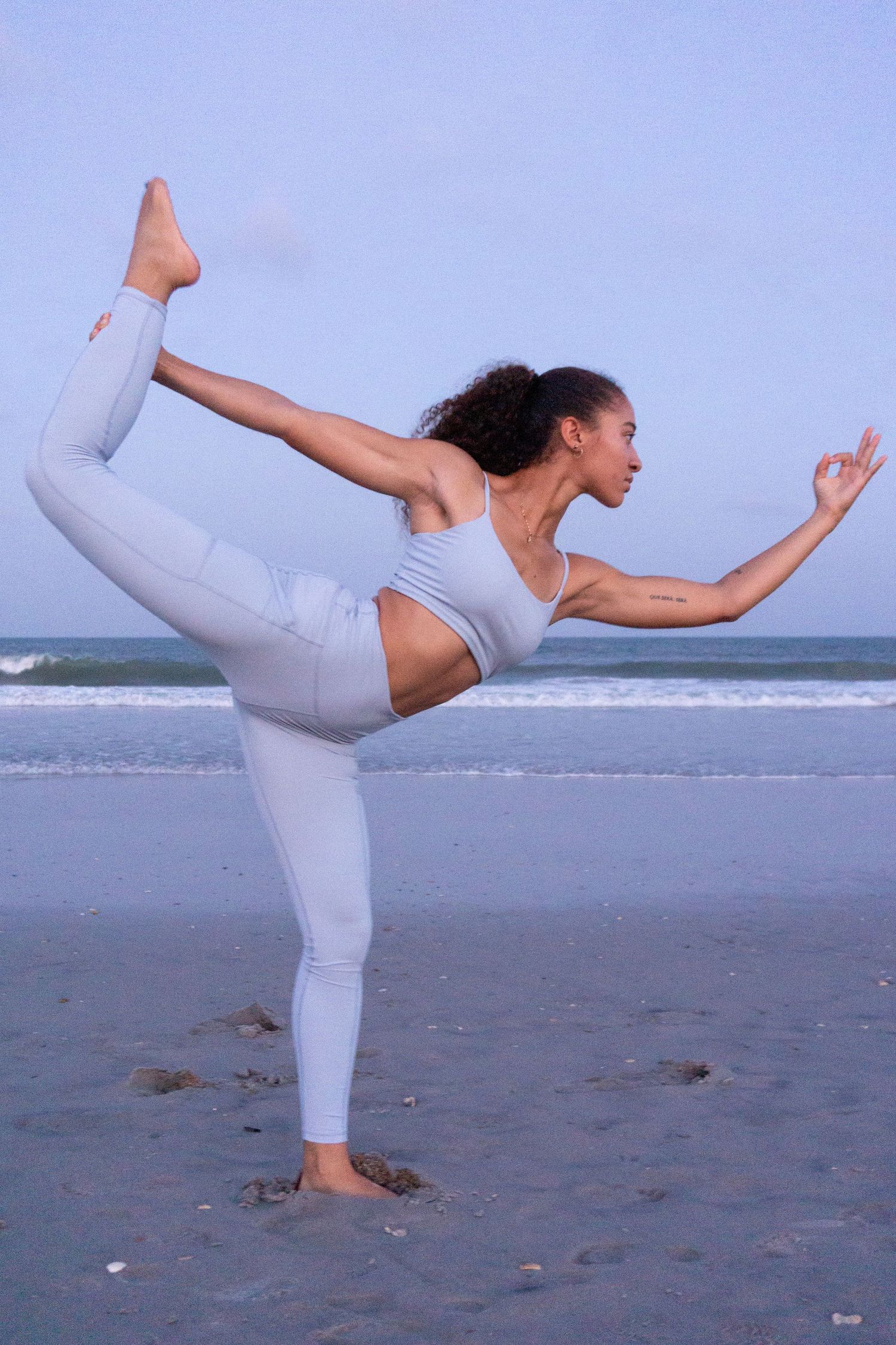 A girl yoga poses on the beach in lilac light purple yoga athletic wear sports bra and leggings