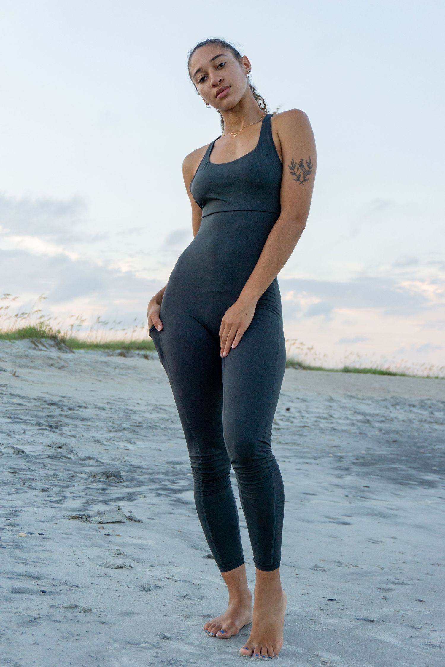 A girl walks on the beach in grey bodysuit yoga athletic wear