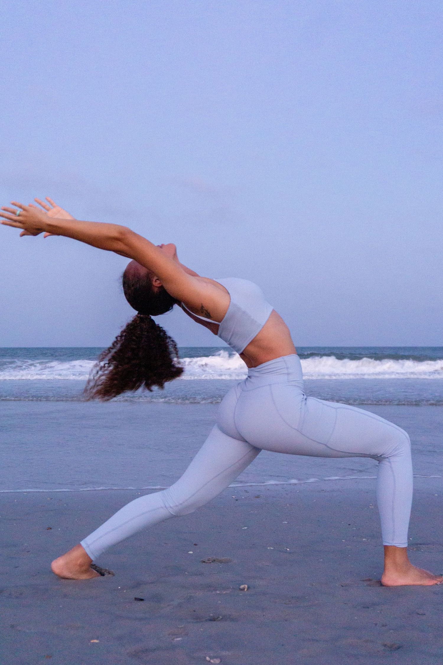 A girl yoga poses on the beach in lilac light purple yoga athletic wear sports bra and leggings