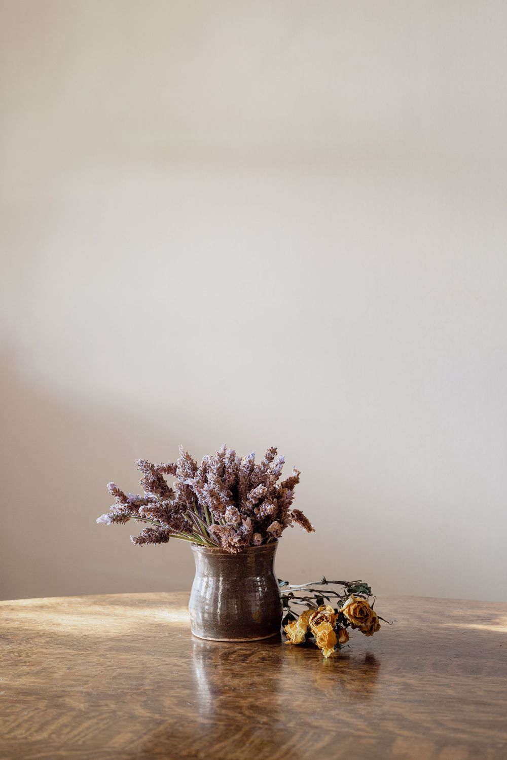 Dried purple flowers in rustic vase on wooden table with soft lighting.