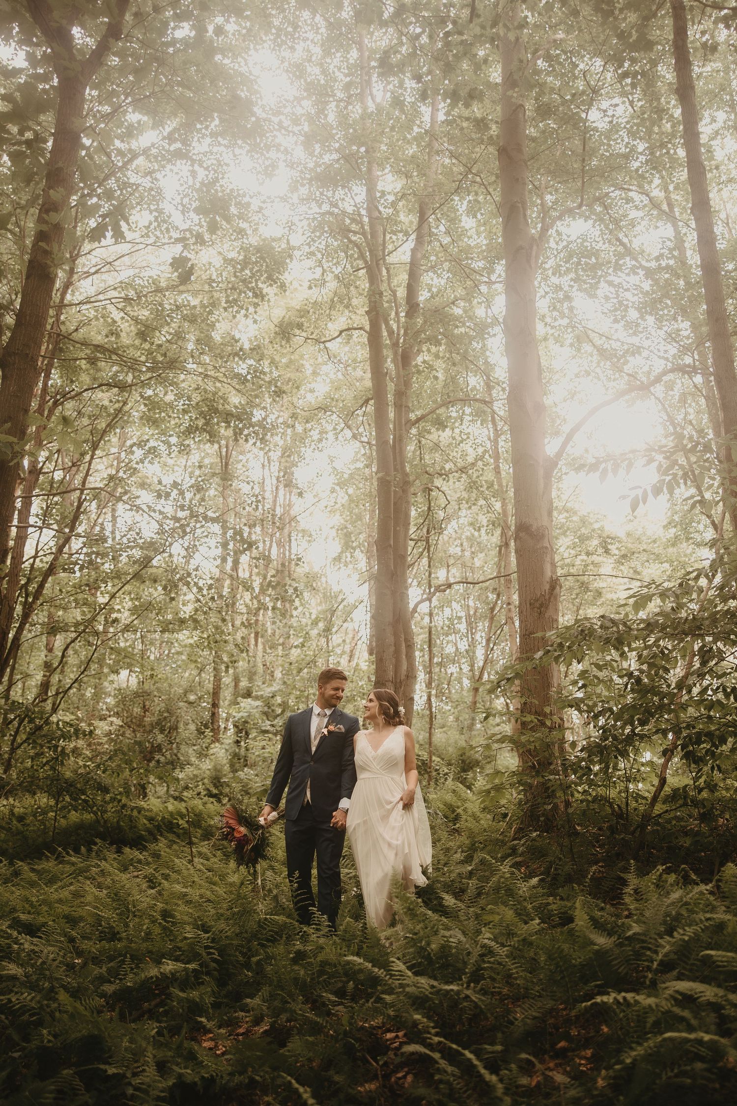Couple walks hand in hand through misty forest in romantic wedding photo.