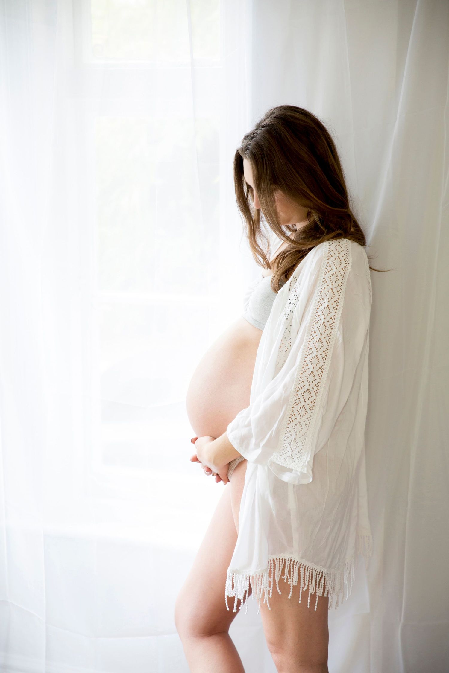 Ethereal maternity photo with white lace robe and natural window light.