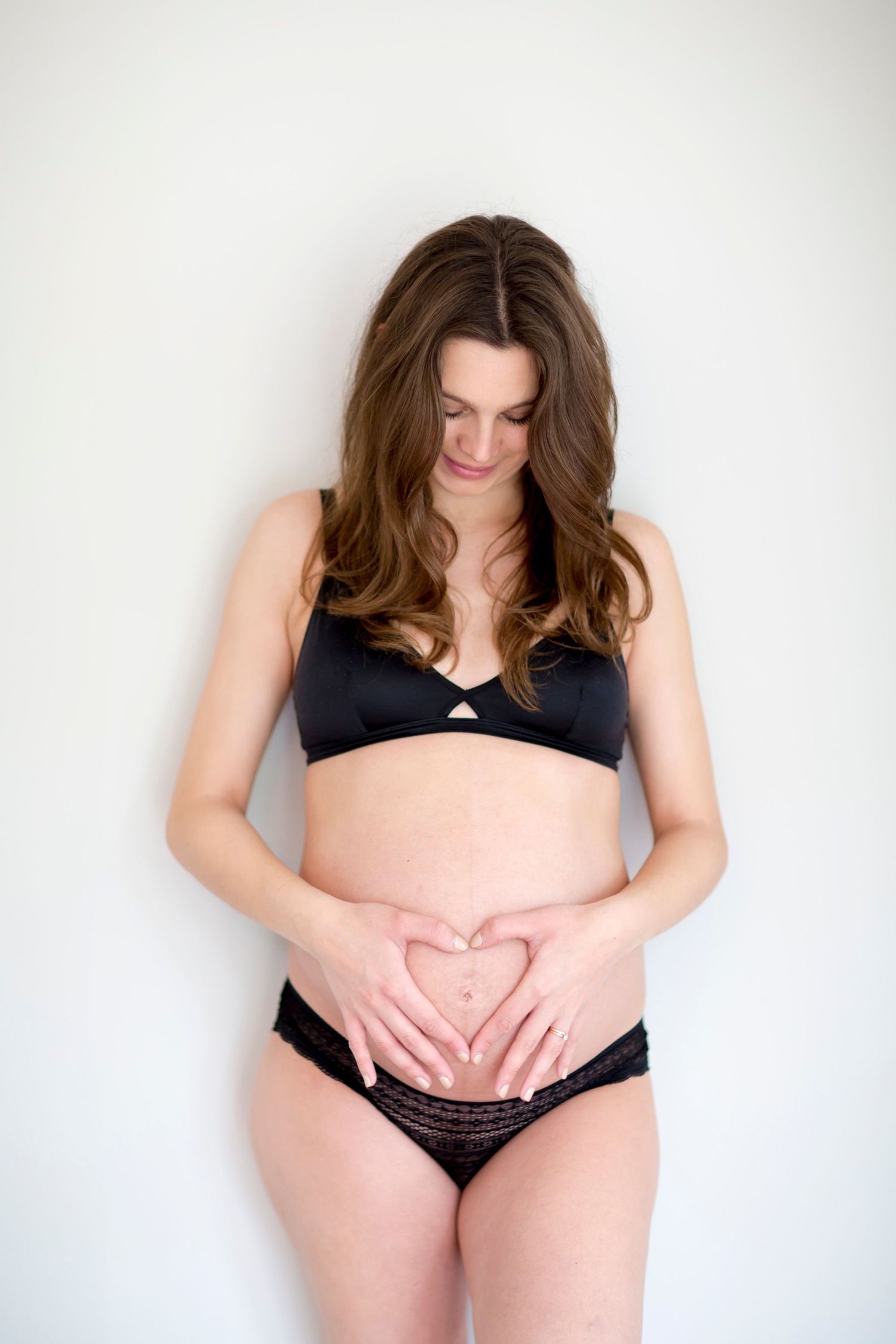 Artistic maternity photo showing hands forming heart shape over pregnant belly.