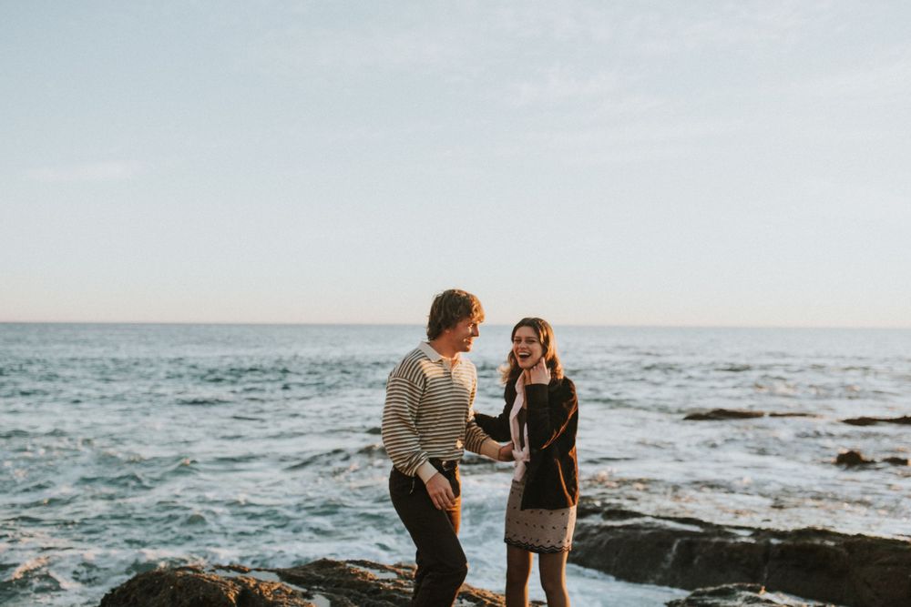Two people share an intimate moment while standing on rocky cliffs by the sea.