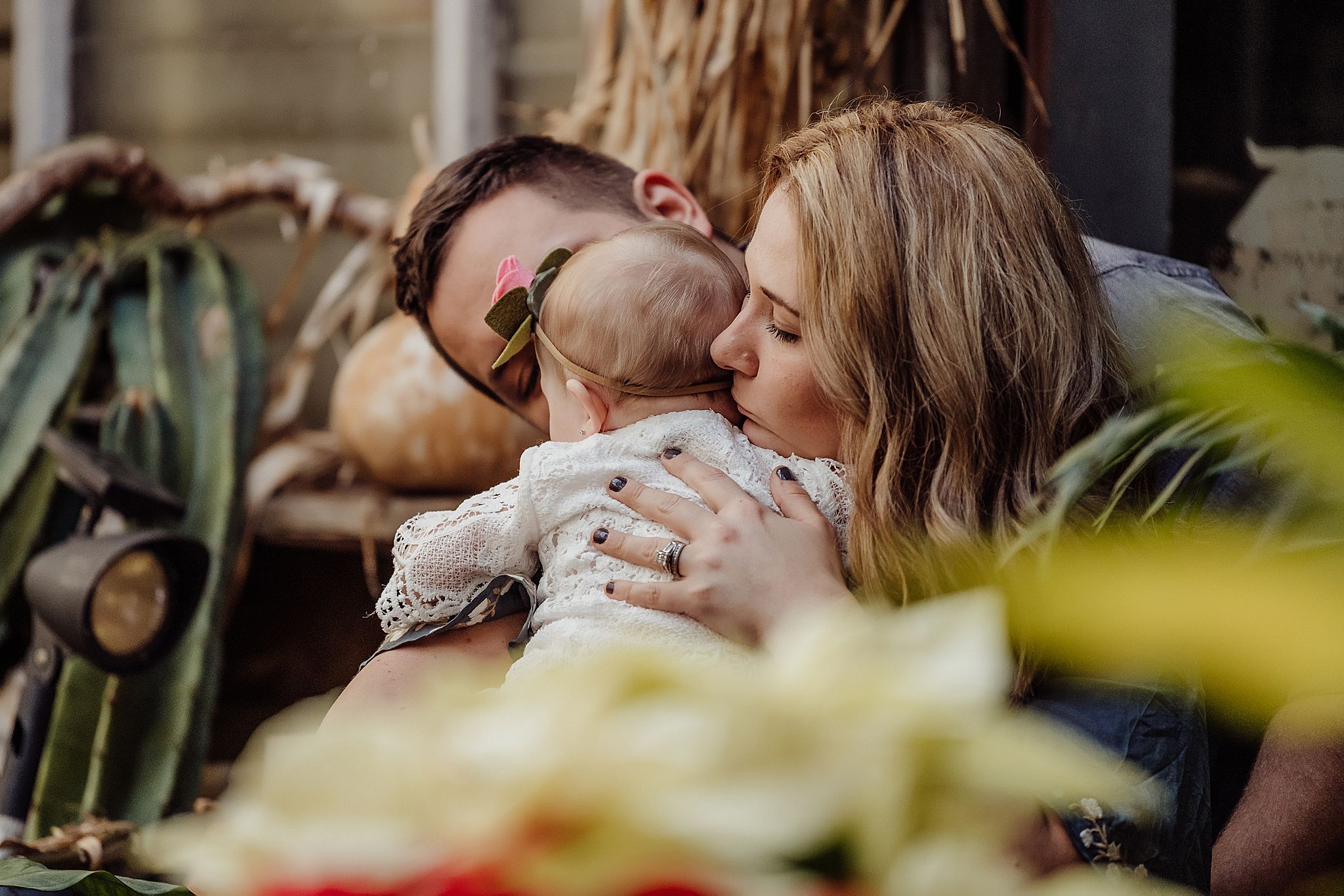 Intimate family moment captured in greenhouse with natural lighting and plants.
