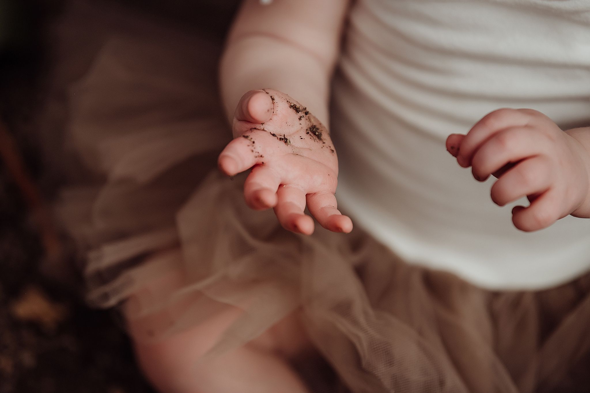 Close-up shot of a tiny infant hand reaching out against a soft brown background.