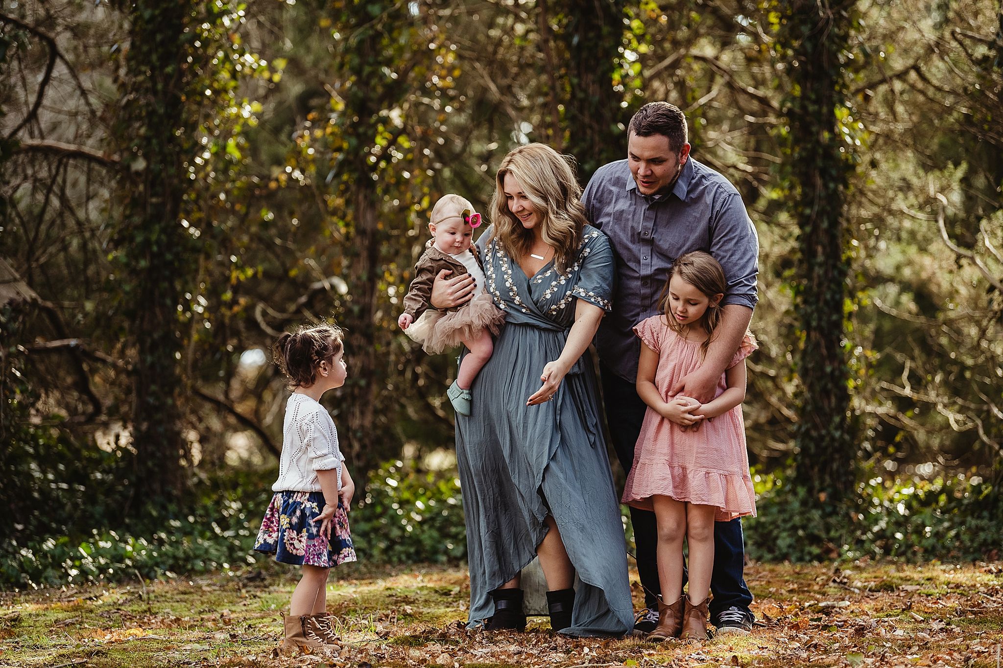 Family portrait in wooded setting with golden sunlight filtering through trees.