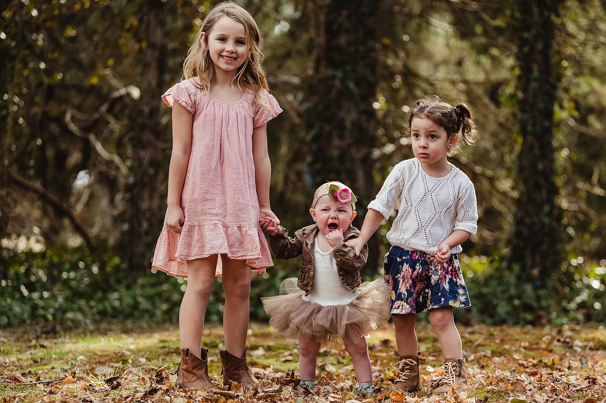 Three children in coordinated outfits playing together on autumn leaves.