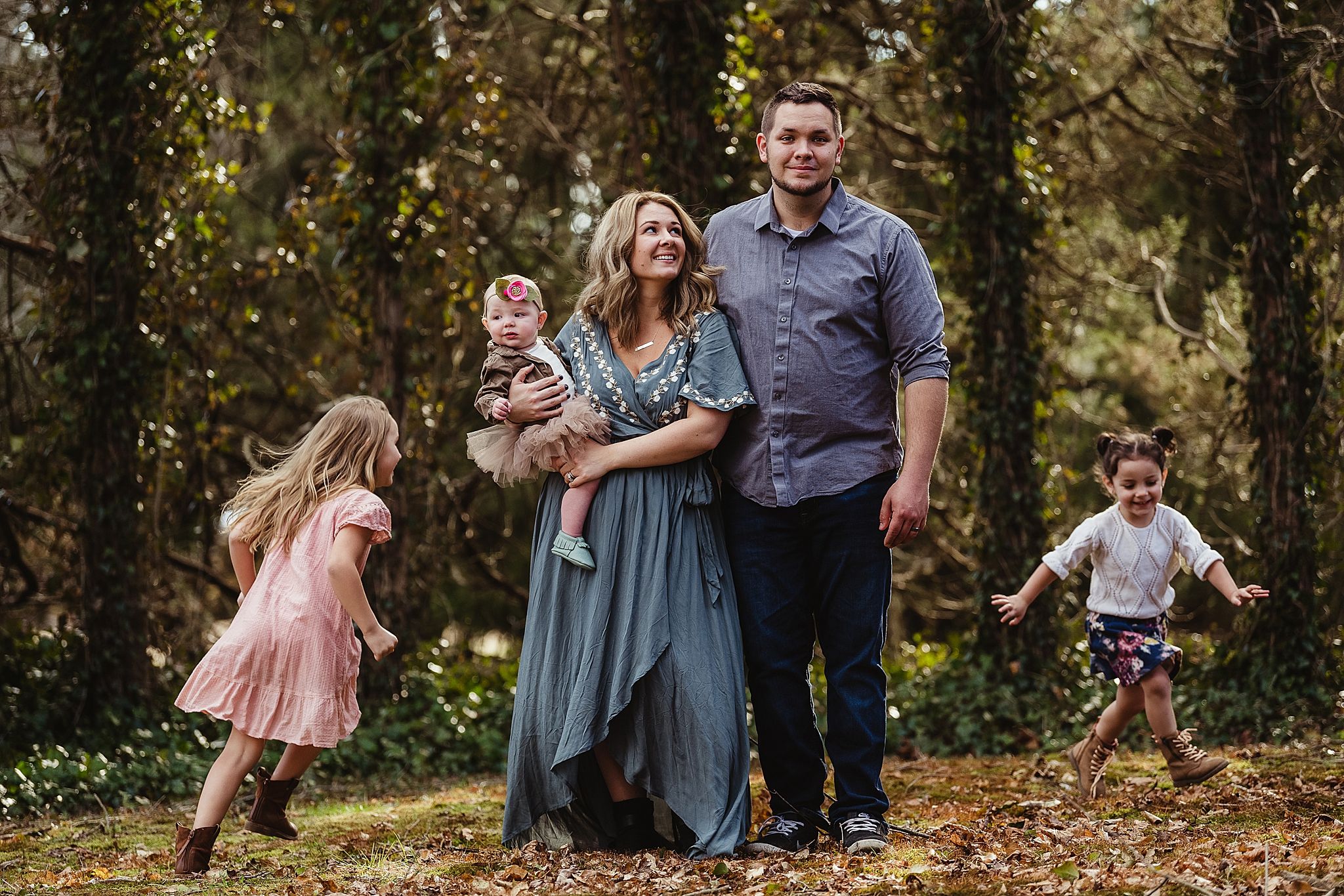 Family enjoying playful moment together in wooded area during golden hour.