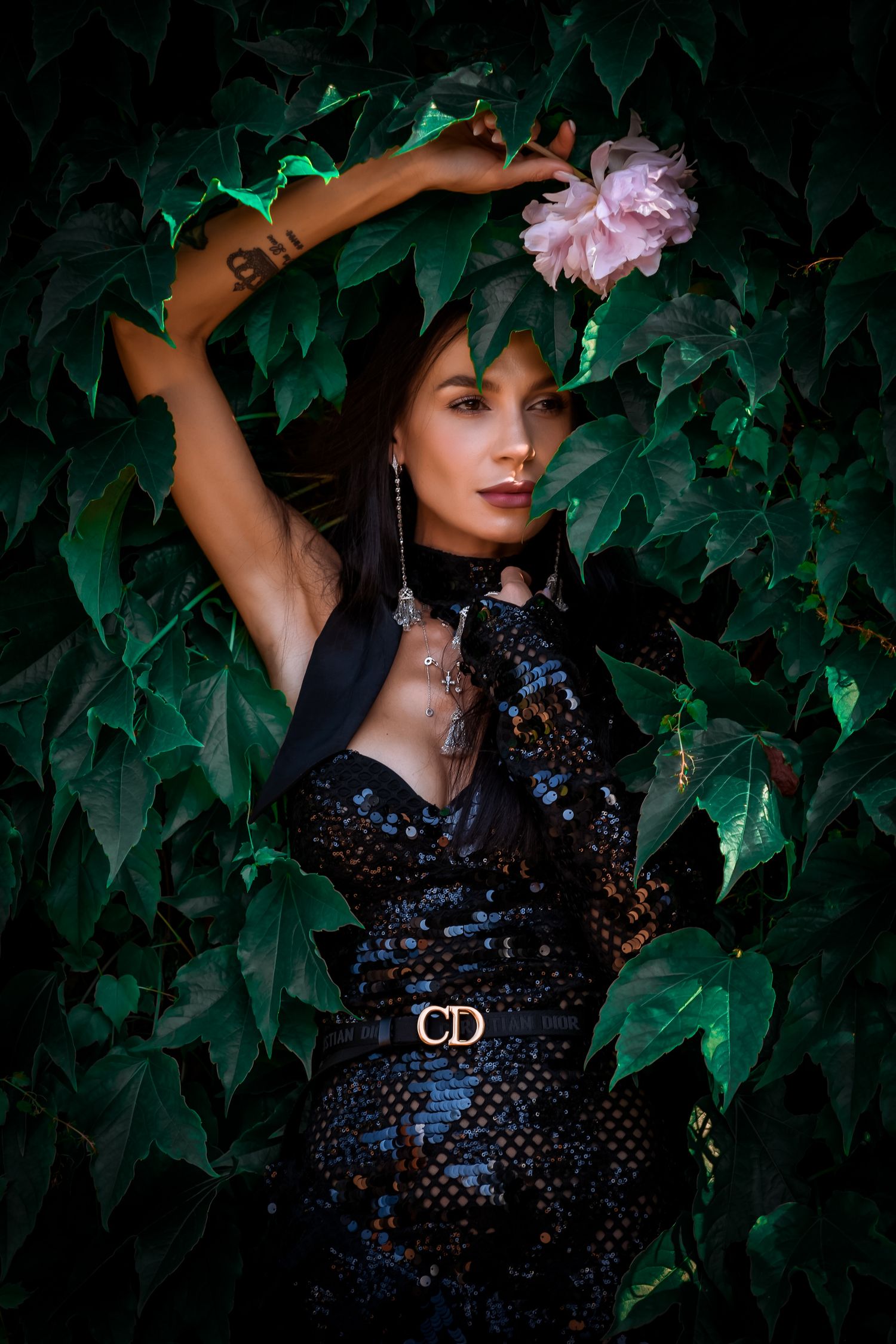 Artistic portrait against ivy backdrop featuring a black sequined dress and pink flower accent.