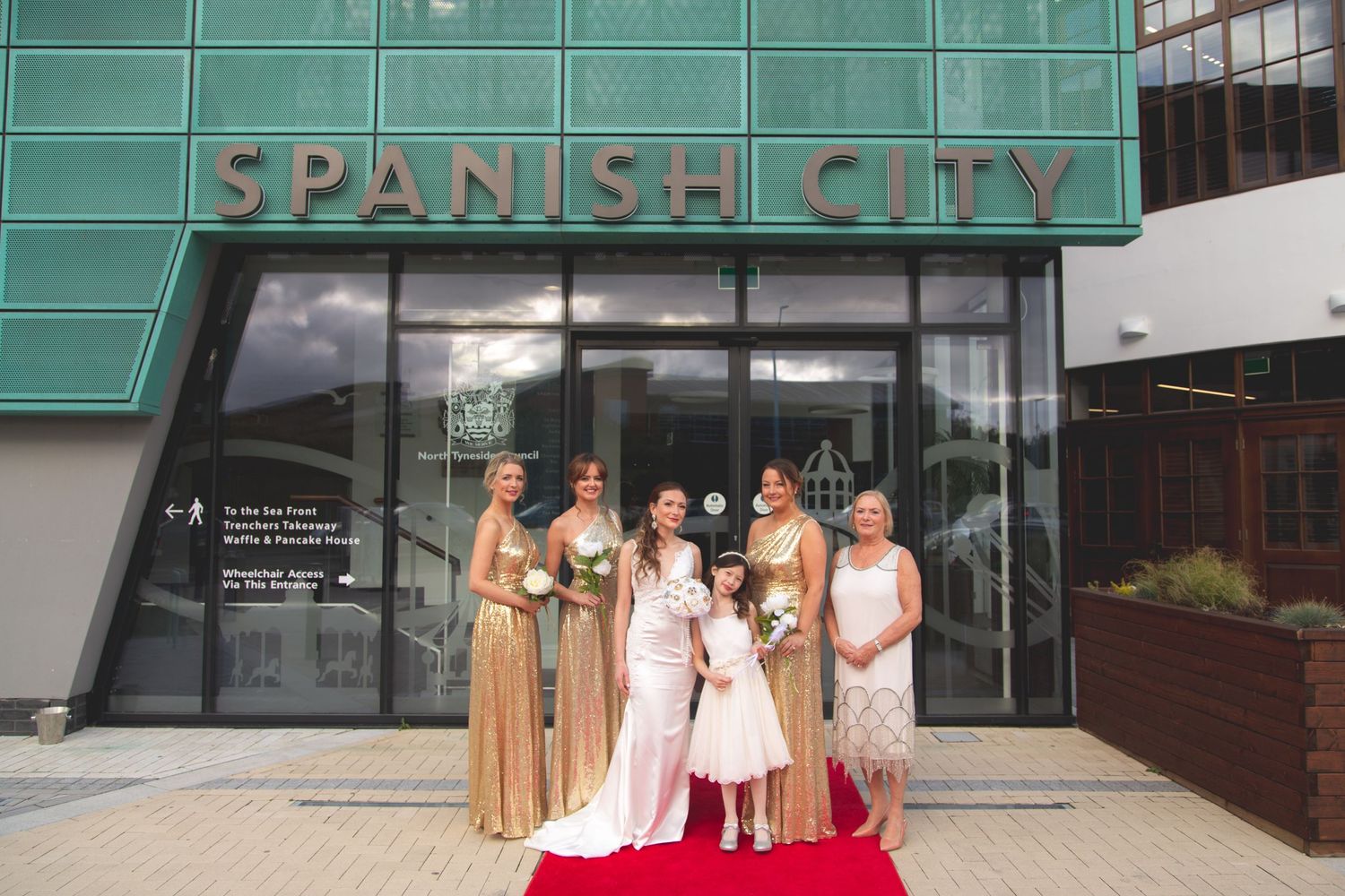 Wedding party in gold and white dresses pose outside Spanish City entrance.