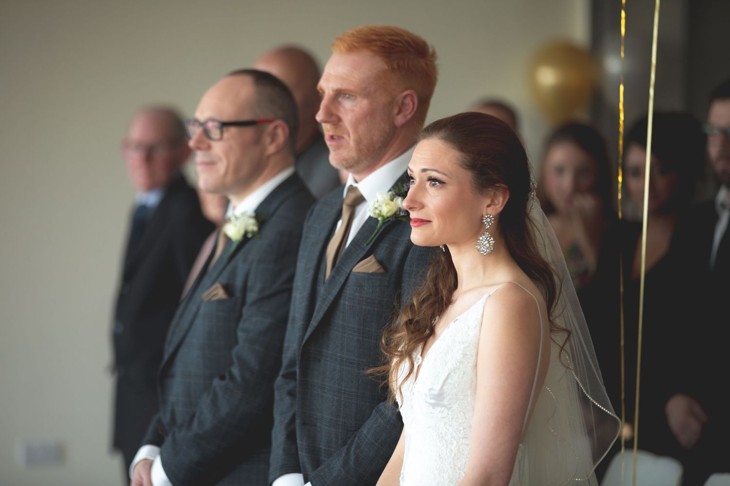 Wedding couple and guests standing during formal ceremony in elegant indoor setting.