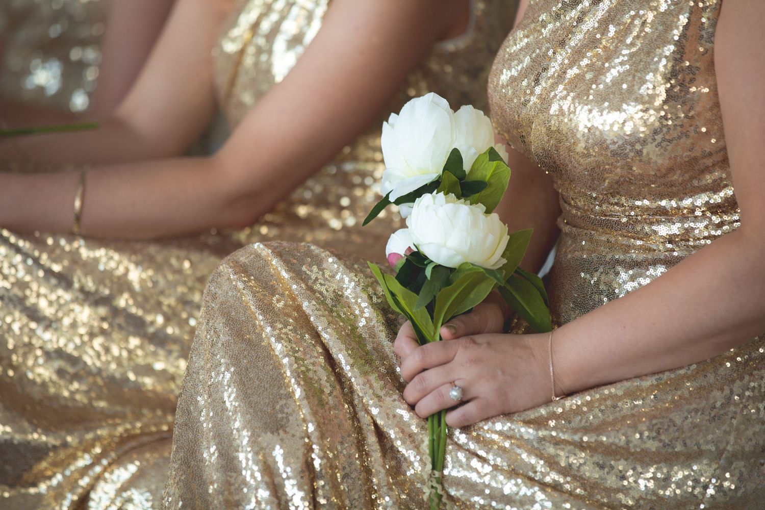 Person holding white flowers while wearing sparkly gold sequined dress.