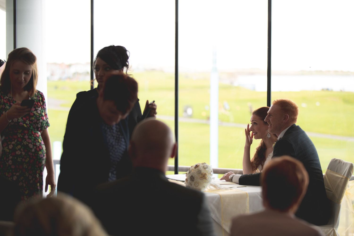Wedding reception guests gathered near large windows with scenic view.