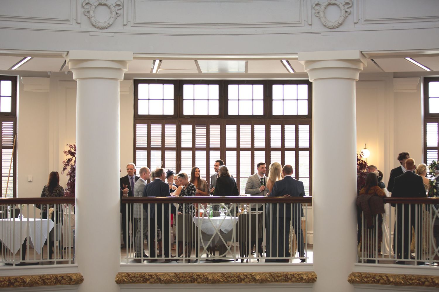 Guests gather on ornate balcony overlooking elegant venue space.