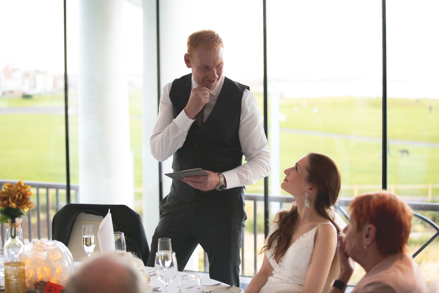Wedding reception speech moment at elegant venue with panoramic windows.