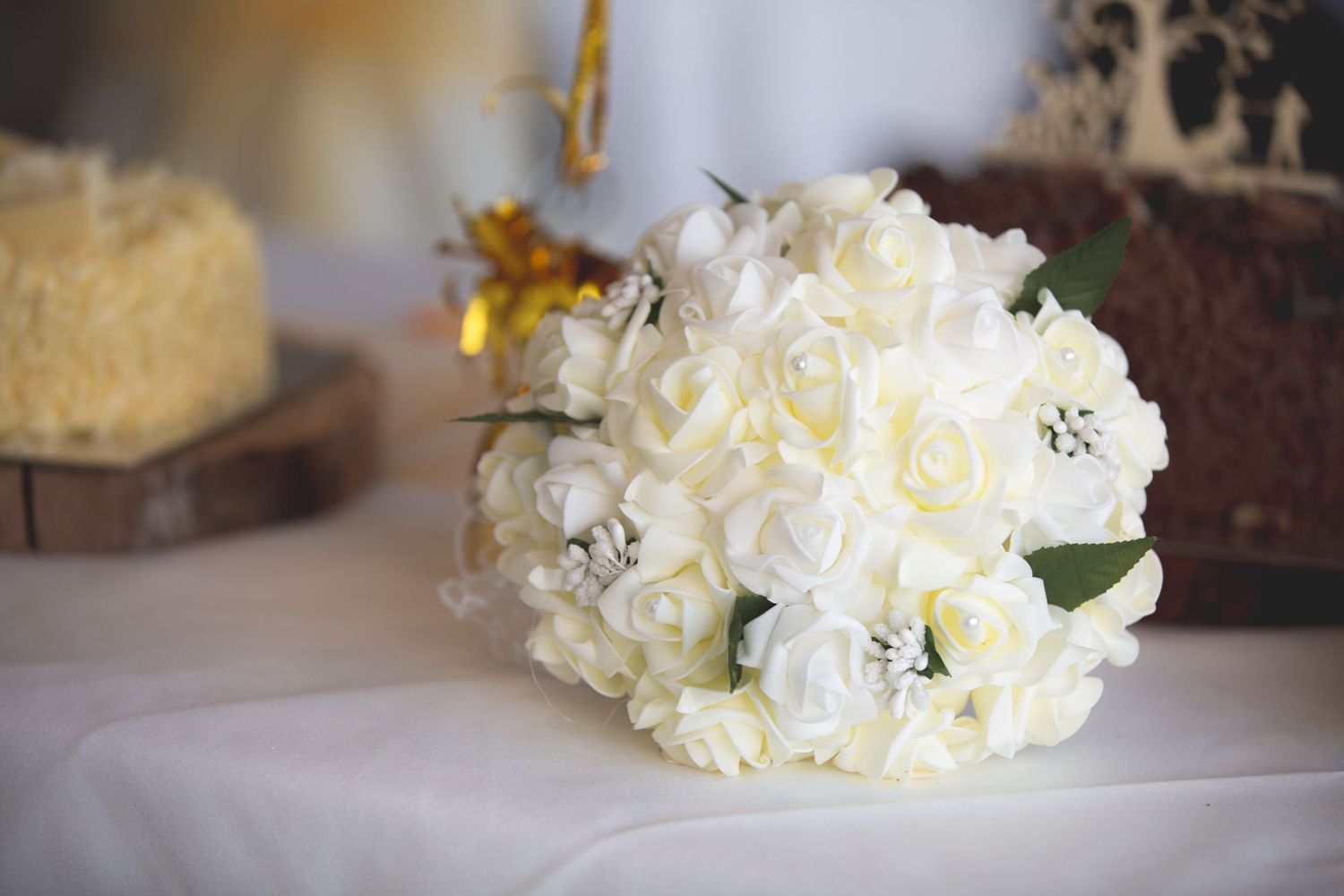 Classic white rose bridal bouquet resting on white linen tablecloth.