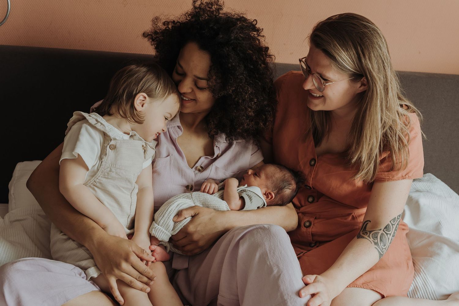 Three people share joyful moment with toddler and newborn on couch.