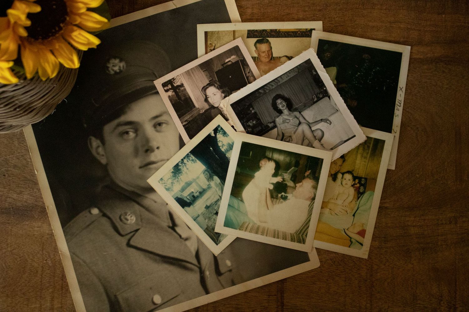 A group of old pictures on a table with a sunflower displayed