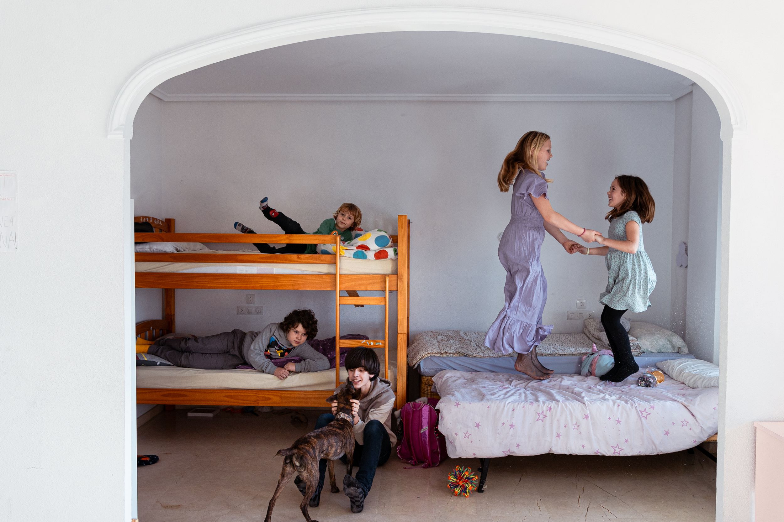 Children playing and jumping on bunk beds and mattresses in a cozy bedroom alcove.
