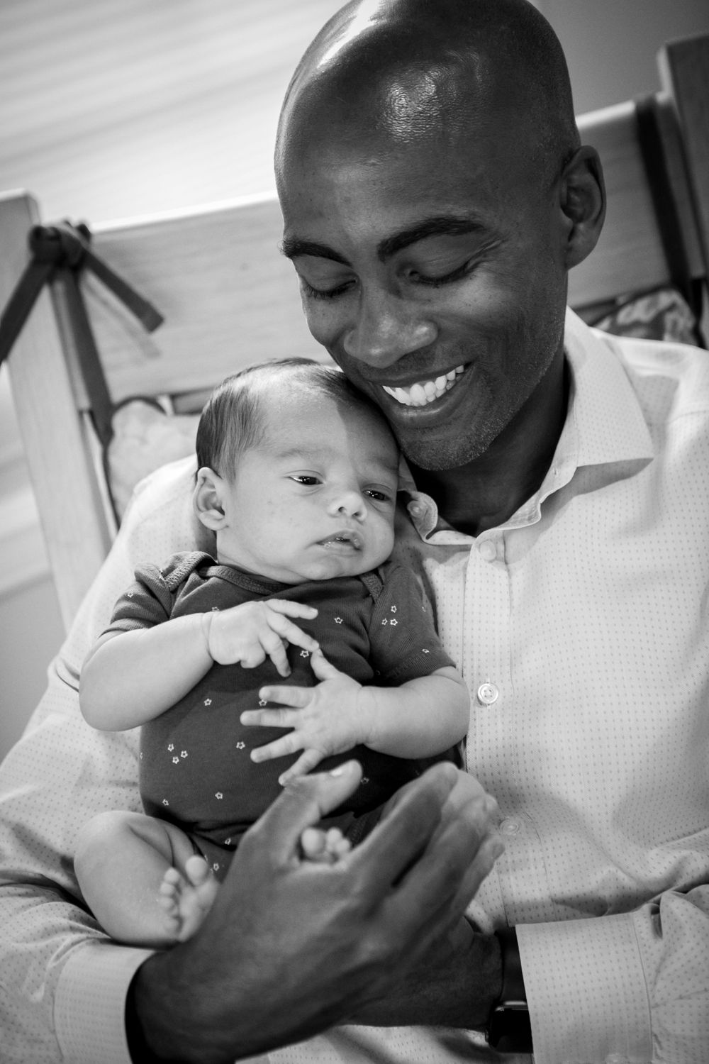 Parent smiling warmly while holding sleepy infant in casual indoor setting.
