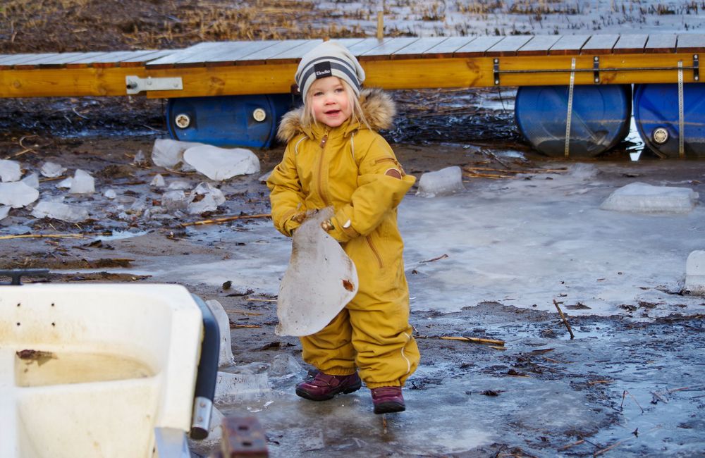 A small figure in a bright yellow rainsuit stands on wet ground near a boat.