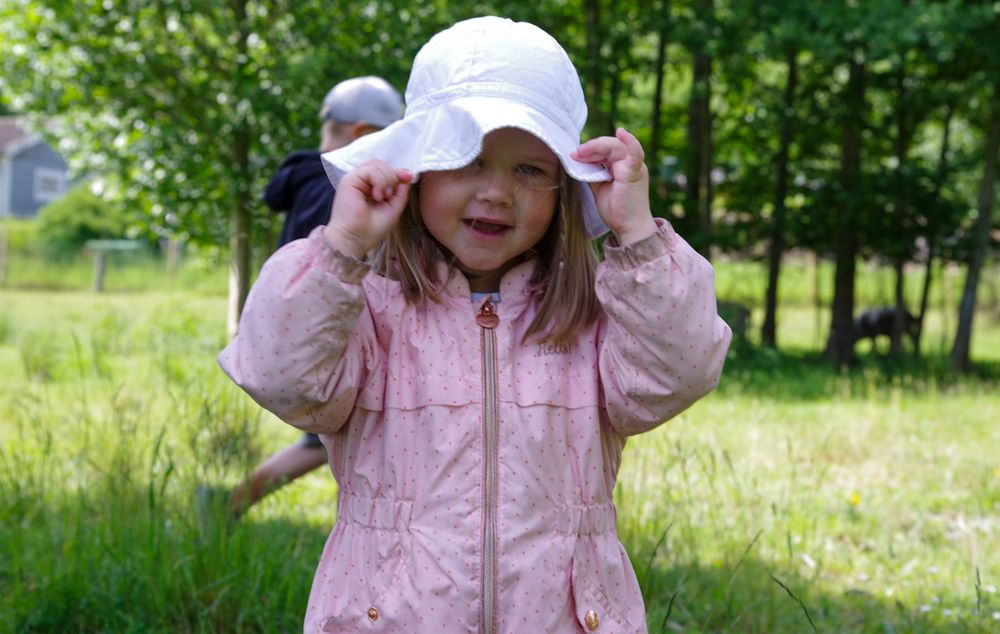 Child in pink jacket and white sunhat plays outdoors on a sunny day.