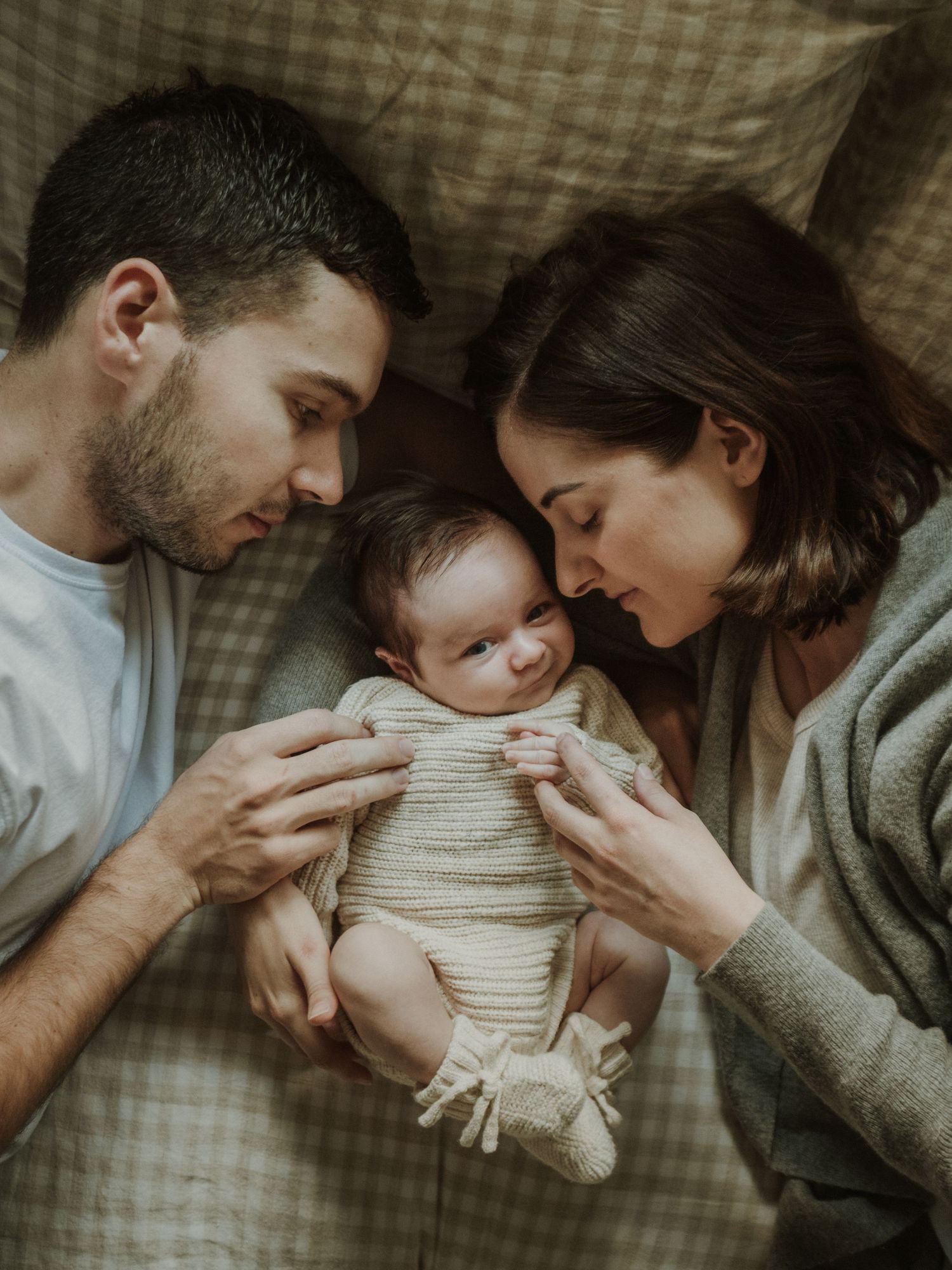 Mother and Father lying on bed cuddling with their newborn baby
