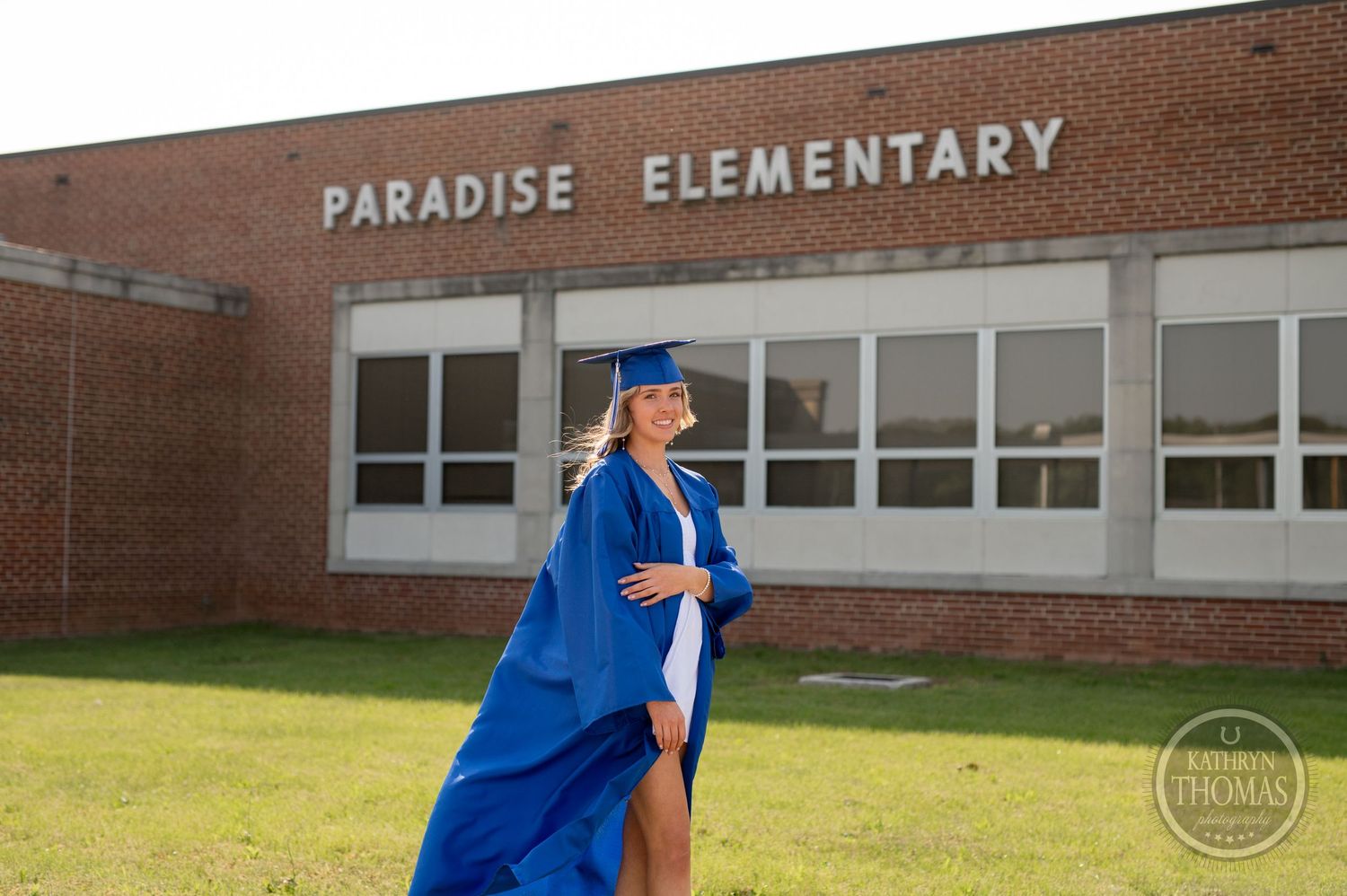 Graduate in blue cap and gown takes photos in front of Paradise Elementary school.