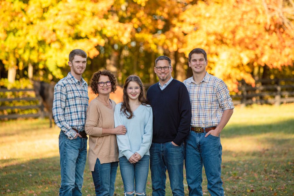 Group portrait in outdoor setting with golden autumn foliage in background.
