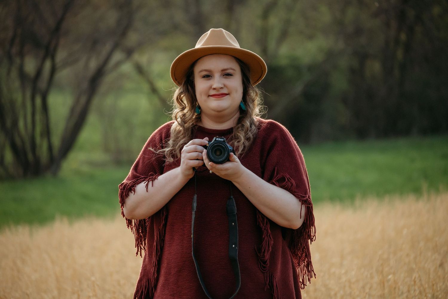 Portrait of a photographer wearing a brown hat and burgundy poncho in a rustic field setting.