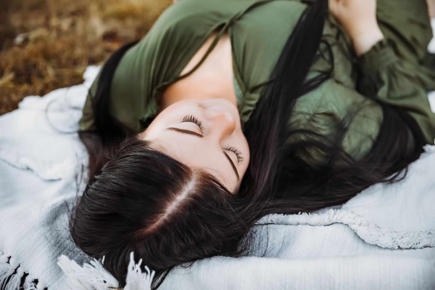 Person with long dark hair lying on ground in olive green jacket.