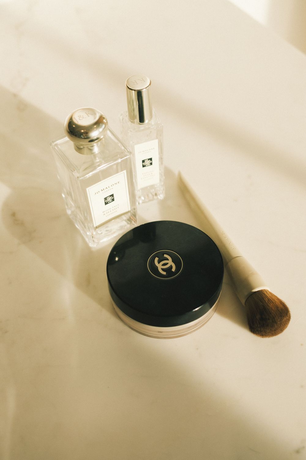 Luxury beauty products and perfume bottles arranged with dramatic shadows on white surface.