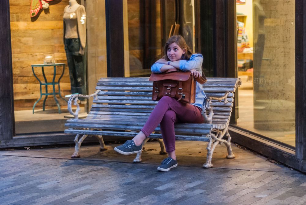 Woman sitting on a bench, leaning on leather messenger bag in downtown Greenville, South Carolina