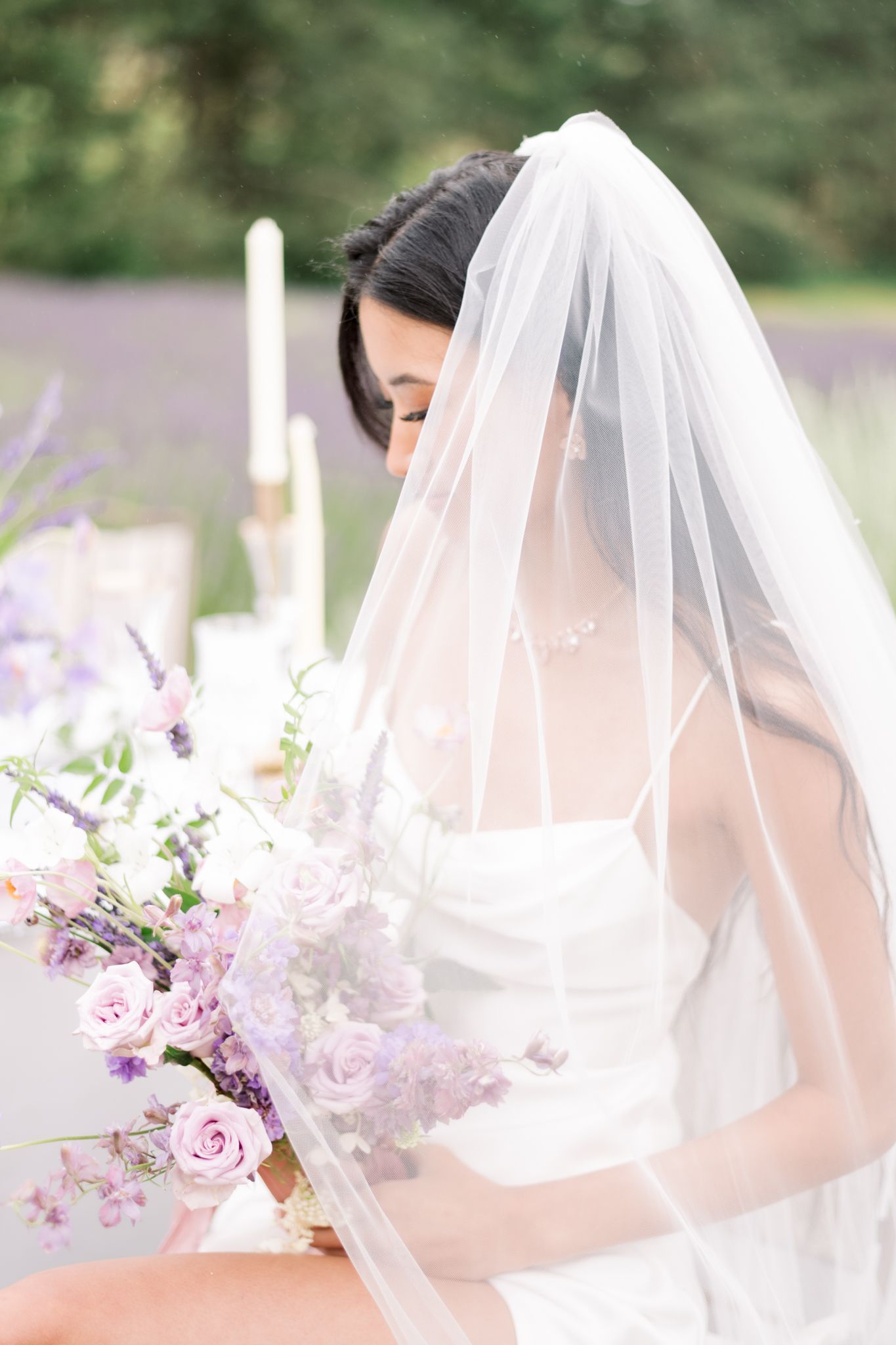 Ethereal bridal portrait with delicate veil and purple floral bouquet in soft lighting.