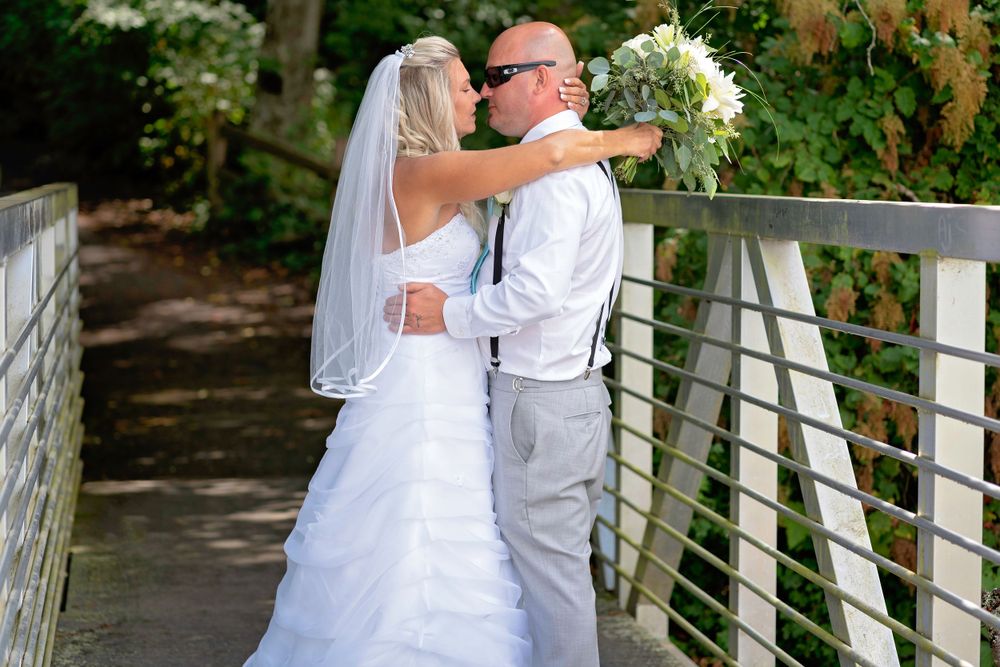 A wedding couple embraces on a wooden bridge surrounded by greenery.