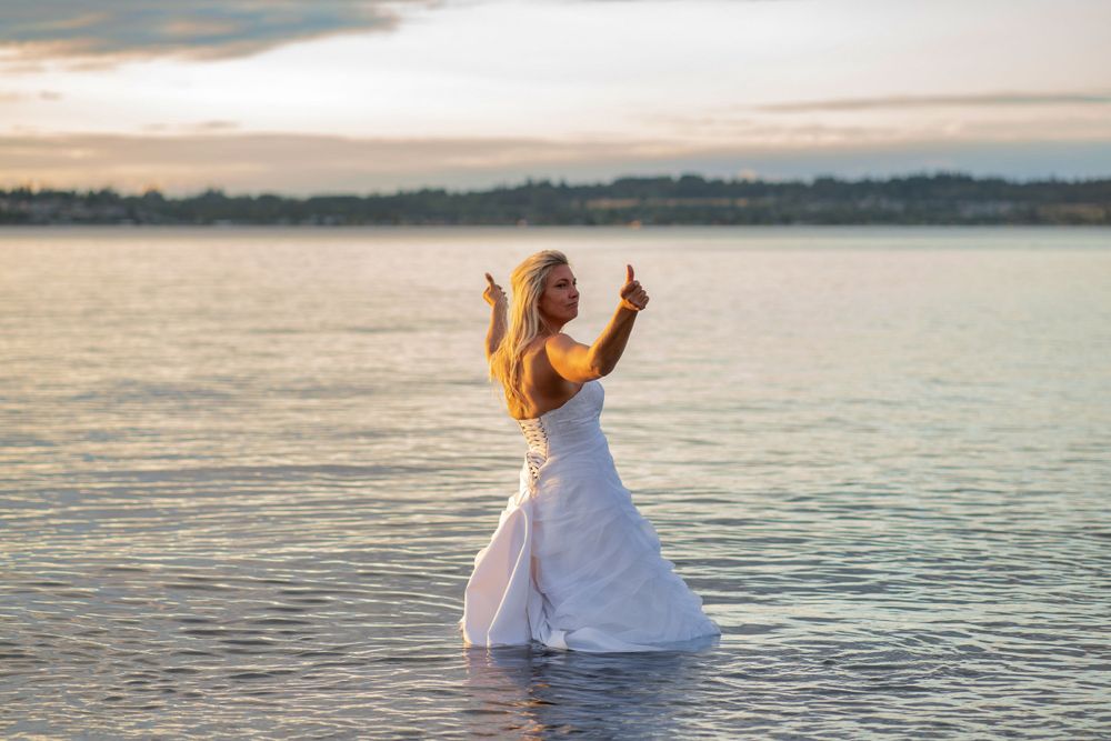 A bride stands in shallow water at sunset wearing her wedding dress.