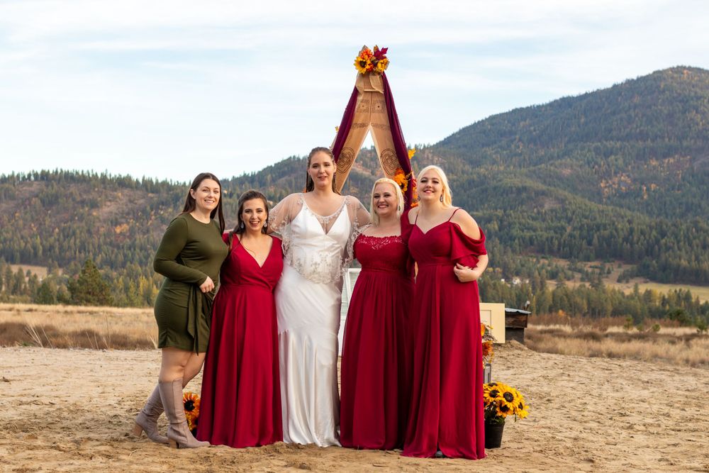 Wedding party with bridesmaids in red dresses poses against mountain landscape.