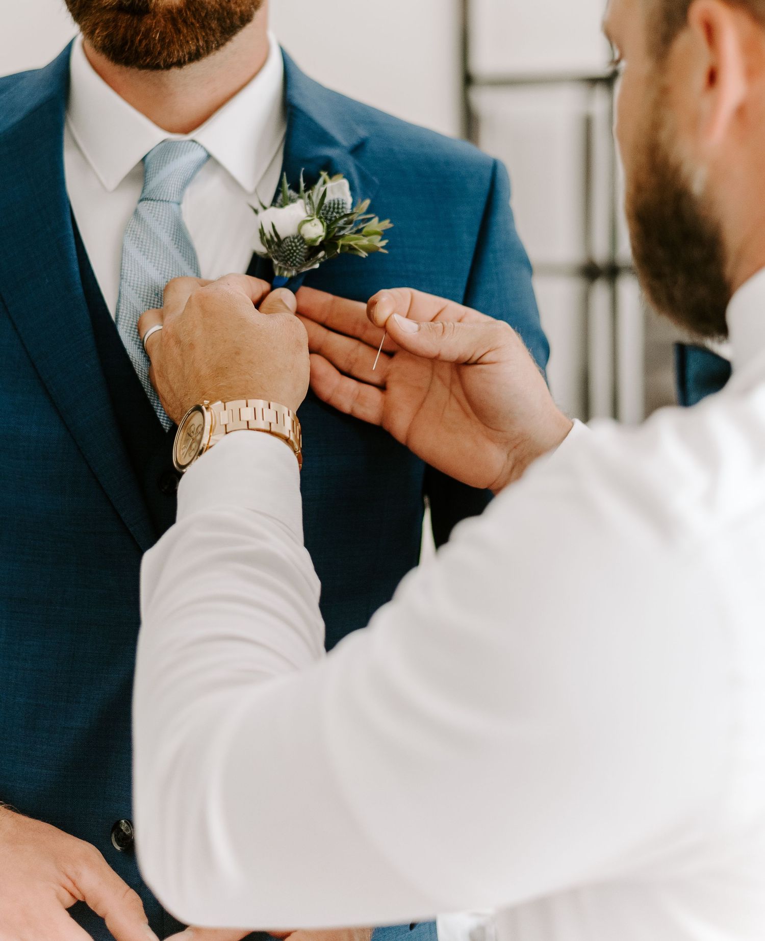 Close-up shot of someone adjusting a blue suit jacket and boutonniere.